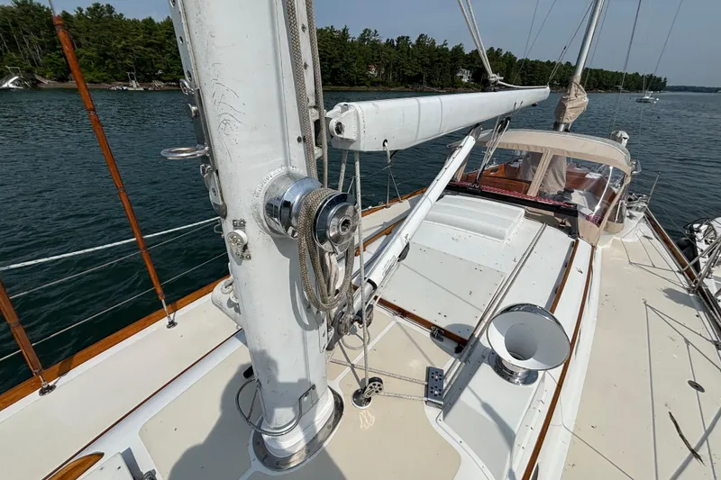 Slide: The Image of 1974 Hinckley Bermuda 40 MKIII sailboat deck with mast and rigging, anchored near forested shoreline. - 10