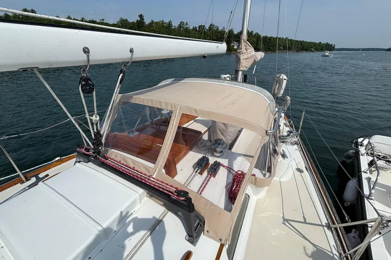 Slide: The Image of 1974 Hinckley Bermuda 40 MKIII sailboat with beige canopy, docked on calm water. - 11
