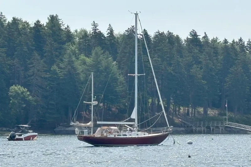 Slide: The Image of A 1974 Hinckley Bermuda 40 MKIII sails near a forested shoreline. - 2