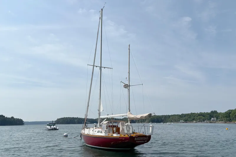 Slide: The Image of 1974 Hinckley Bermuda 40 MKIII sailboat anchored on a calm lake under a clear sky. - 6