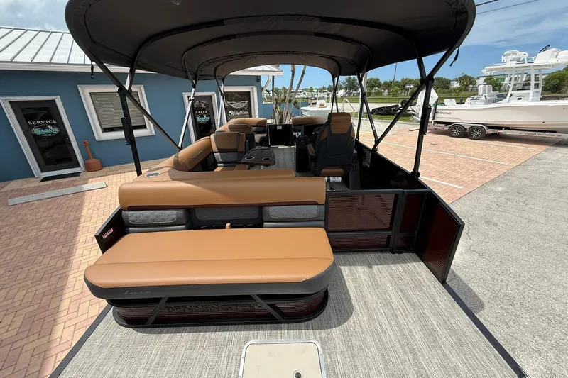 Slide: The Image of 2026 Bennington 21 SLJ pontoon boat with tan seating and canopy, parked at a marina. - 5