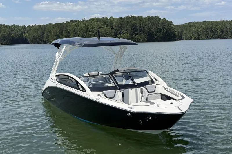 The Image of A sleek 2021 Yamaha 275SD boat on a calm lake with a wooded shoreline. - 0
