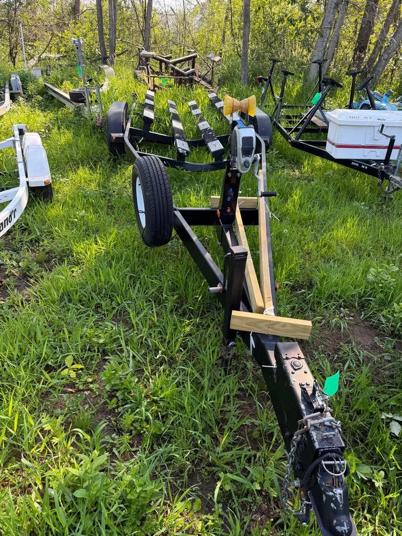 Slide: The Image of Boat trailer on grassy terrain, surrounded by trees. The trailer has a spare tire and a winch. - 16