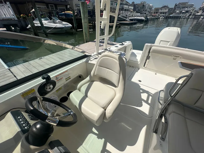 Slide: The Image of The image shows the cockpit of a 2018 Boston Whaler 230 Vantage. It features white seats and a modern steering wheel. Boats and a dock are visible in the background. - 14