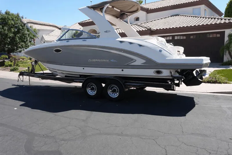Slide: The Image of A 2008 Chaparral 264 Sunesta on a trailer in front of a house. The boat has a sleek design. - 2