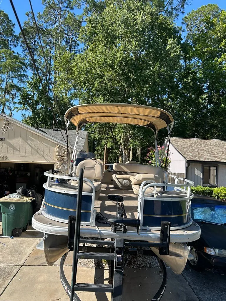 Slide: The Image of A Sun Tracker Bass Buggy pontoon boat on a trailer in a driveway, surrounded by trees. - 17