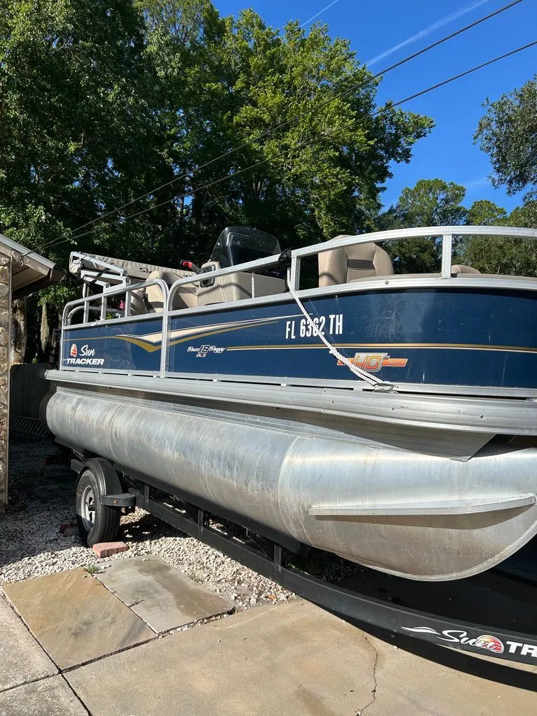 Slide: The Image of A 2023 Sun Tracker Bass Buggy pontoon boat on a trailer in a yard. - 2