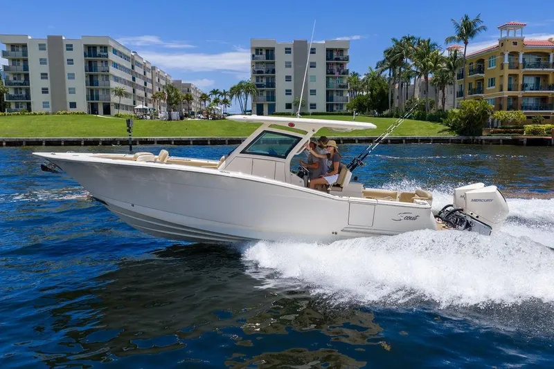 Slide: The Image of 2021 Scout 305 LXF boat cruising on water near waterfront buildings. - 14