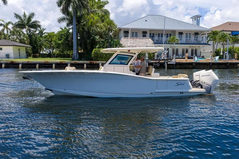 Slide: The Image of 2021 Scout 305 LXF boat cruising on a sunny waterfront near luxury homes. - 11