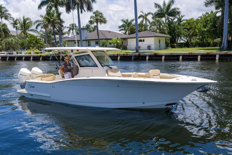 Slide: The Image of 2021 Scout 305 LXF boat cruising on a sunny waterway with palm trees. - 7