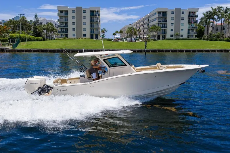 The Image of 2021 Scout 305 LXF boat cruising on water near waterfront buildings. - 0