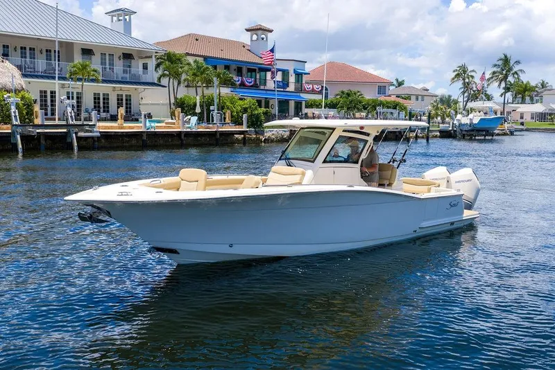 Slide: The Image of 2021 Scout 305 LXF boat cruising near waterfront homes on a sunny day. - 10