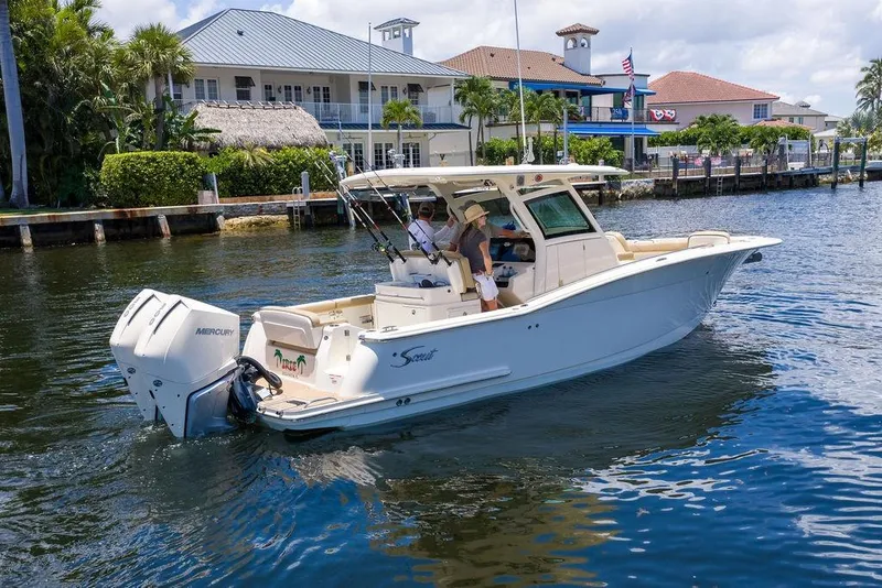 Slide: The Image of 2021 Scout 305 LXF boat cruising on a sunny waterfront near luxury homes. - 1