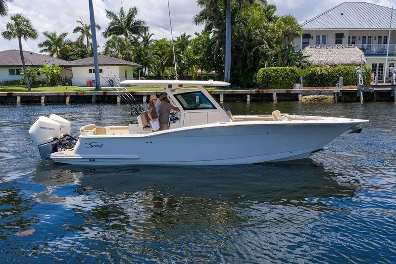 Slide: The Image of 2021 Scout 305 LXF boat cruising on a sunny day near waterfront homes. - 6