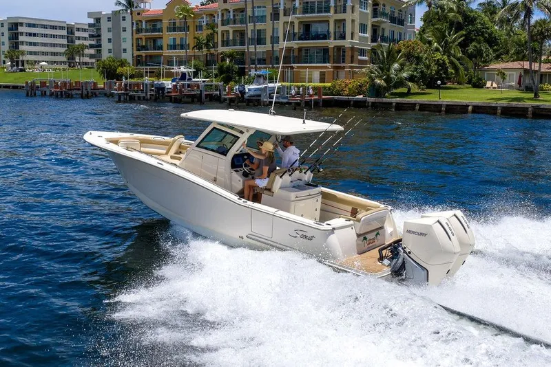 Slide: The Image of 2021 Scout 305 LXF boat cruising on a sunny waterfront near luxury apartments. - 13