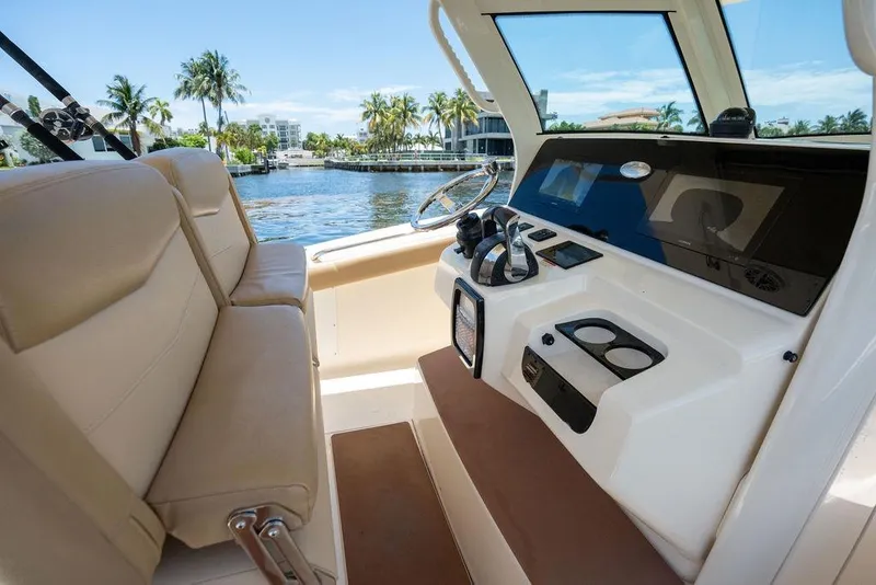Slide: The Image of 2021 Scout 305 LXF boat interior with helm, beige seating, and waterfront view. - 28