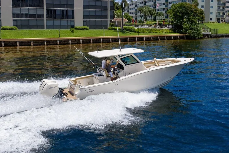 Slide: The Image of 2021 Scout 305 LXF boat cruising on a sunny day near waterfront buildings. - 8