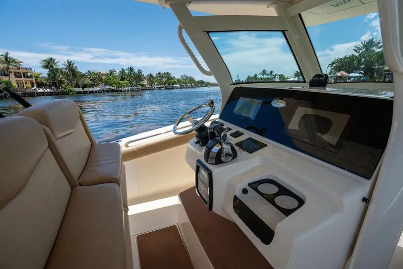 Slide: The Image of 2021 Scout 305 LXF boat interior with steering wheel and dashboard, overlooking scenic waterfront. - 35