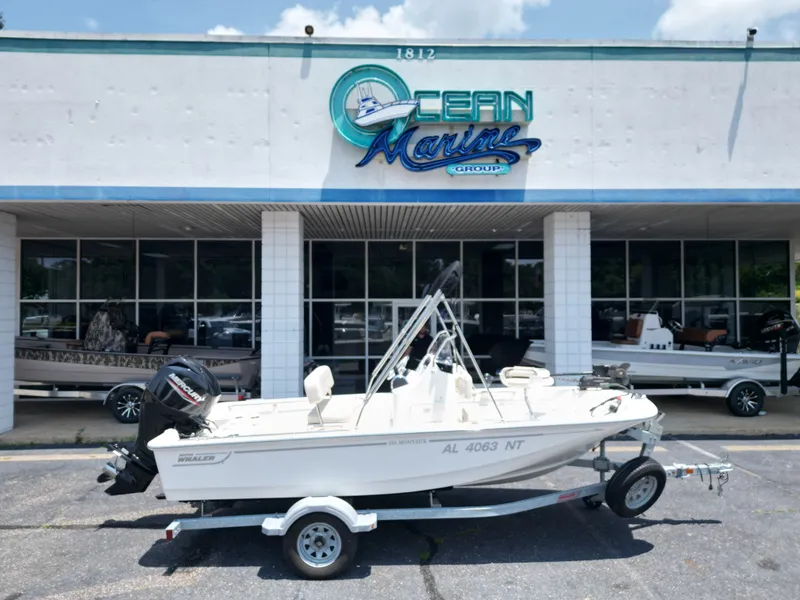 The Image of A 2023 Boston Whaler 150 Montauk on a trailer in front of a building with "Ocean Marine Group" signage. - 1