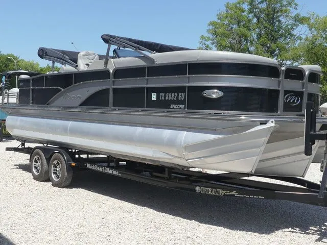 Slide: The Image of A silver pontoon boat on a trailer, surrounded by trees and gravel. - 4