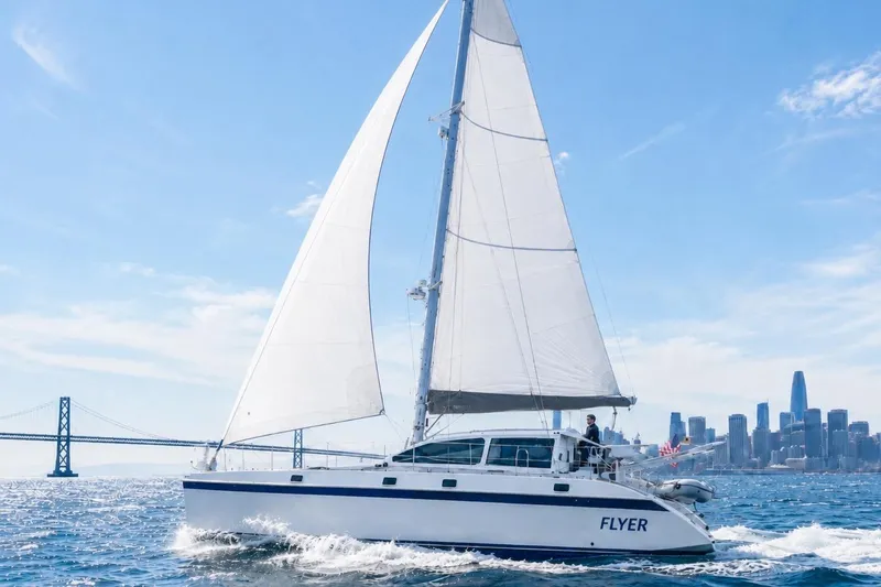 The Image of Sailing catamaran "Visiona" by Baltec Engineering, 1999, cruising near a city skyline and bridge. - 1