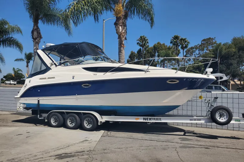 Slide: The Image of 2004 Bayliner 285 boat on trailer, parked outdoors with palm trees in the background. - 1