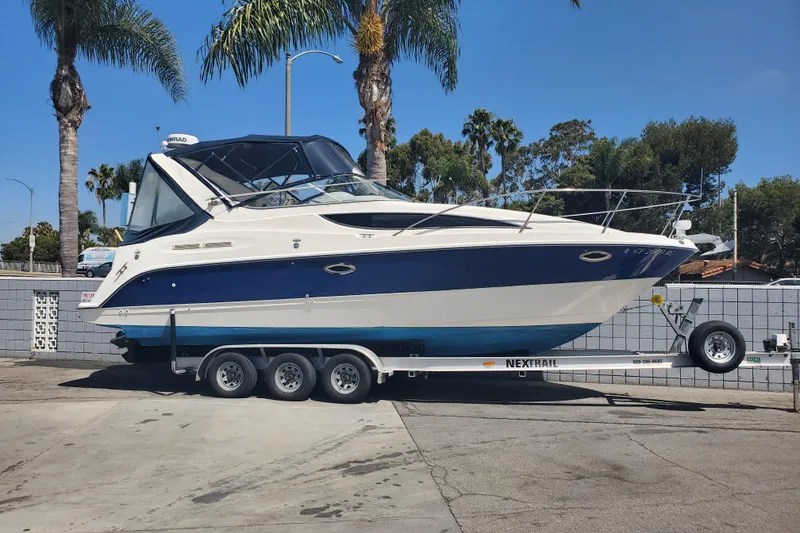 The Image of 2004 Bayliner 285 boat on trailer, parked outdoors with palm trees in the background. - 0