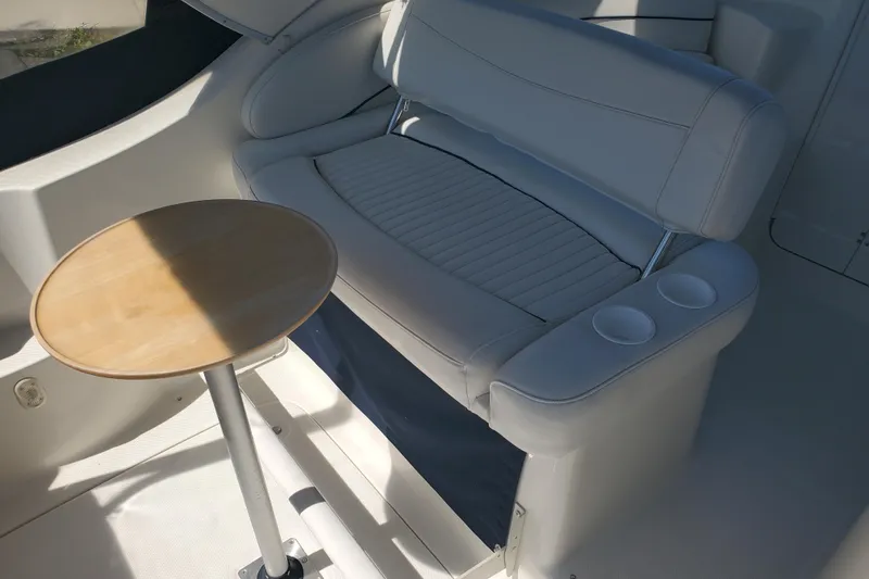 Slide: The Image of Interior of a 2004 Bayliner 285 boat featuring a cushioned seat and small wooden table. - 21