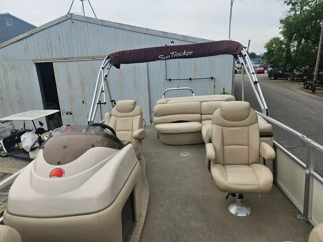 Slide: The Image of A 2008 Tracker Regency Party Barge with beige seating and a sunshade, parked beside a building. - 18