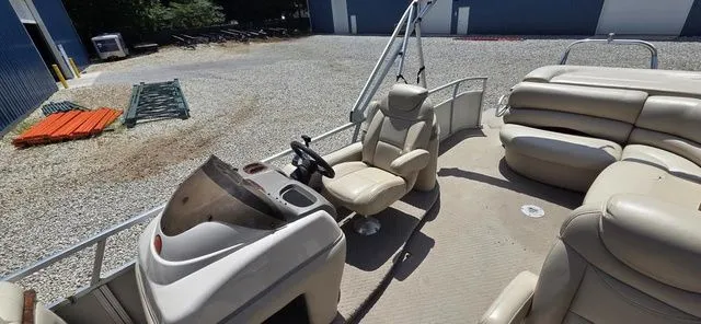 Slide: The Image of A 2008 Tracker Regency Party Barge with beige seating and a helm station on a gravel lot. - 5