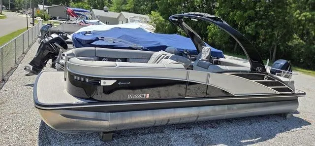 The Image of A 2020 Bennington 25 RXSBA pontoon boat is parked on gravel, surrounded by other boats. - 1