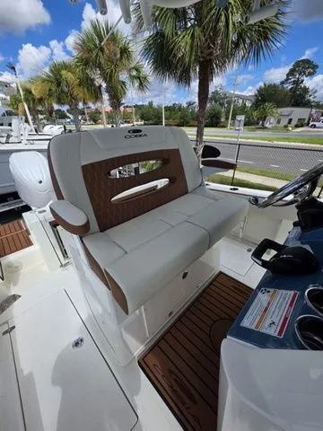 Slide: The Image of The 2027 Cobia 245CC features a white and brown bench seat with palm trees in the background. - 15