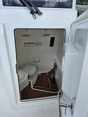 Slide: The Image of The image shows the interior of a 2027 Cobia 245CC boat with a toilet and wood flooring. - 20