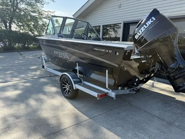 Slide: The Image of A black Smoker Craft Phantom 18 X2 boat from 2027 on a trailer beside a building. - 3