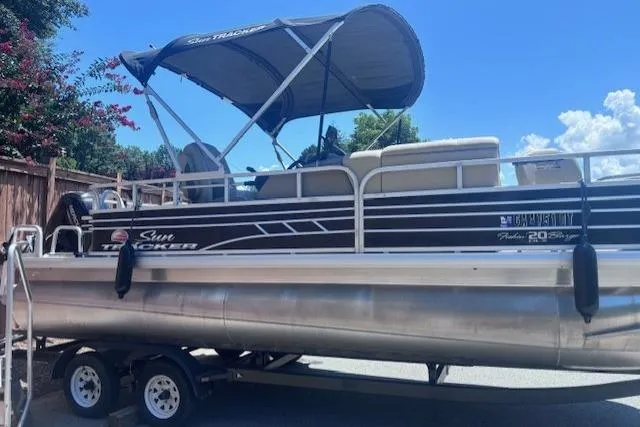 The Image of 2021 Sun Tracker Fishin' Barge 20 DLX pontoon boat on trailer, parked outdoors. - 0