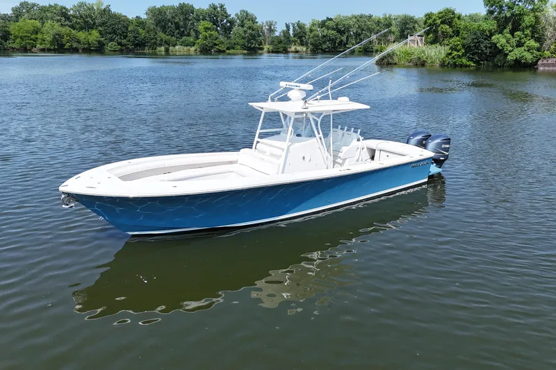 The Image of A blue and white 2010 Regulator 34SS floats on calm water, surrounded by green trees. - 0