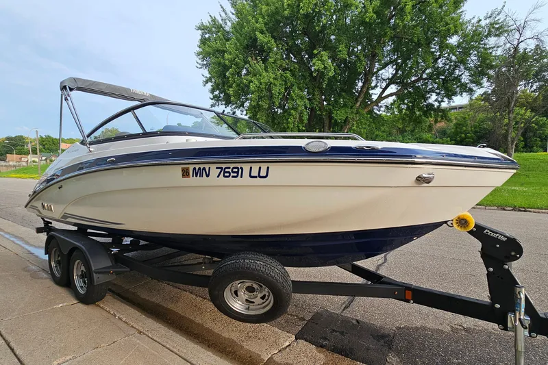 Slide: The Image of 2019 Yamaha Boats 212 Limited on trailer, parked on street with lush greenery. - 4
