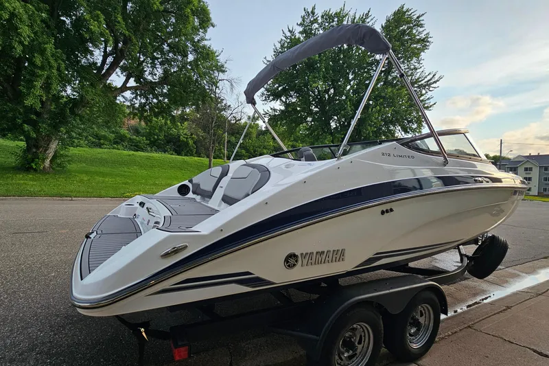 Slide: The Image of 2019 Yamaha Boats 212 Limited on trailer, parked near lush green trees. - 3