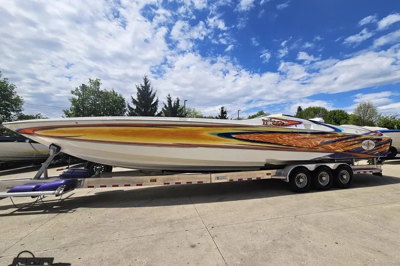 Slide: The Image of 2002 Cigarette 42' Tiger boat with vibrant graphics on a trailer under a blue sky. - 24