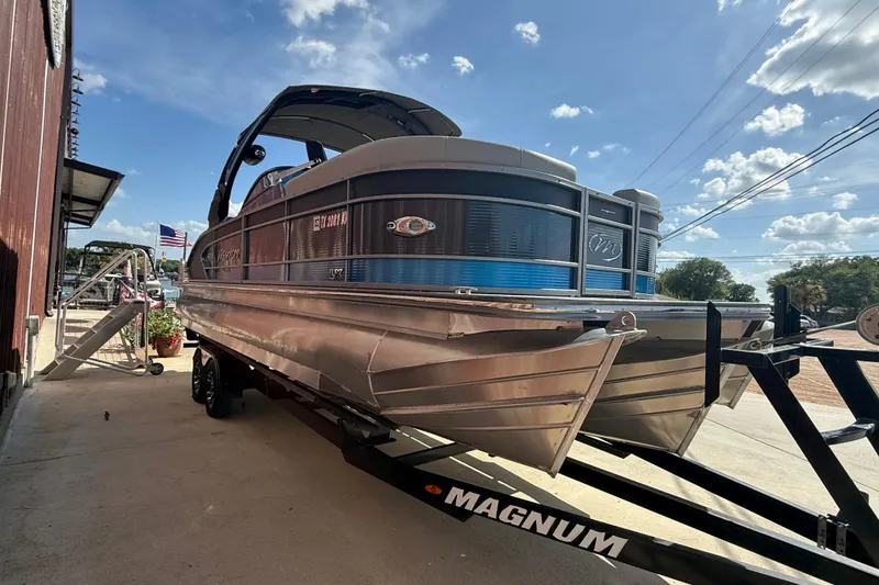 Slide: The Image of 2023 Manitou 25LXSHP pontoon boat on trailer, sunny day, American flag in background. - 3