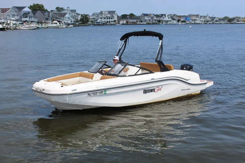 Slide: The Image of A 2022 Bayliner DX 2000 cruising on calm water. Houses are visible in the background. - 5
