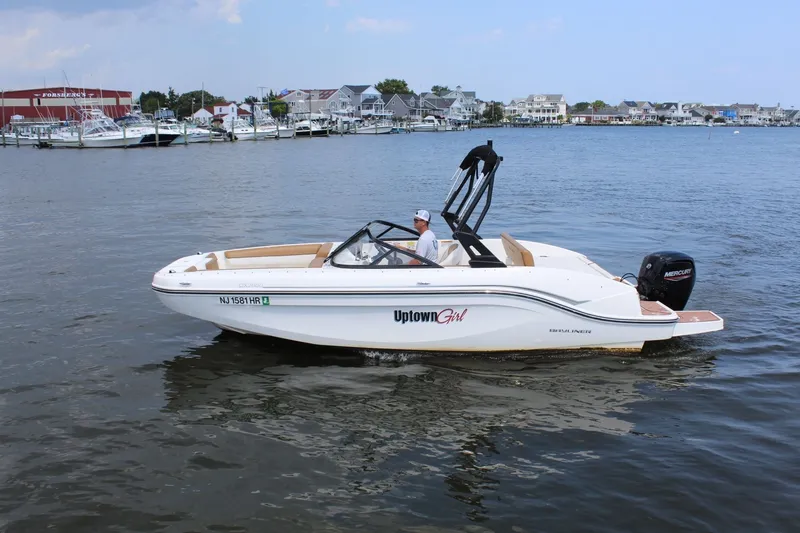 Slide: The Image of A 2022 Bayliner DX 2000 cruising on calm water. Houses and boats are visible in the background. - 6