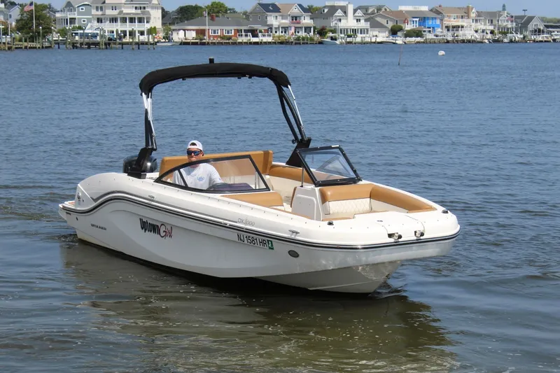 Slide: The Image of A 2022 Bayliner DX 2000 cruising on calm waters. Houses are visible in the background. - 2