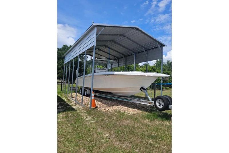 Slide: The Image of 2003 Dakota 36 CC boat under metal shelter on trailer, grassy area, clear sky. - 6
