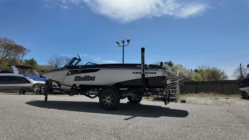 Slide: The Image of A 2025 Malibu TXi boat on a trailer in a parking lot under a blue sky. - 5