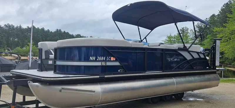 Slide: The Image of Sylvan Mirage X5 CLZ 2026: Sleek pontoon boat with blue hull and canopy, on a trailer. - 1