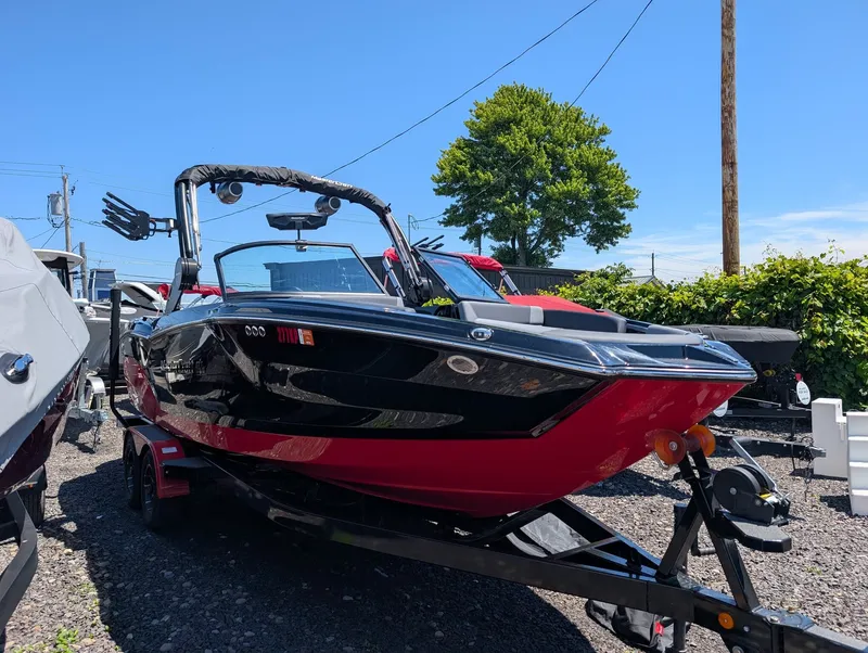 The Image of A 2025 MasterCraft NXT 23 boat with a red and black hull sits on a trailer. - 1