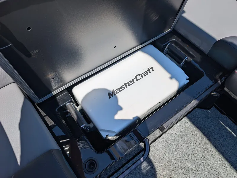 Slide: The Image of An open storage compartment on a MasterCraft NXT 23 boat reveals a white container with the MasterCraft logo. - 12