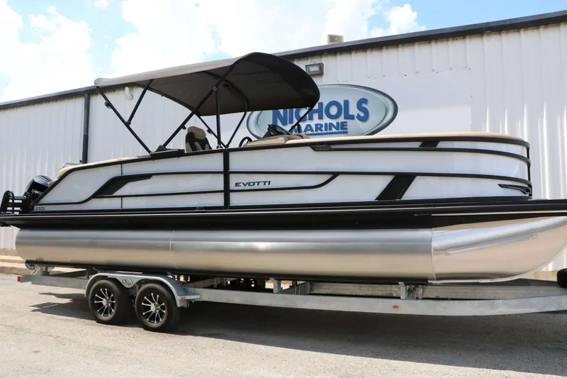 Slide: The Image of A 2026 Evotti 725 QL pontoon boat on a trailer in front of a building. - 2
