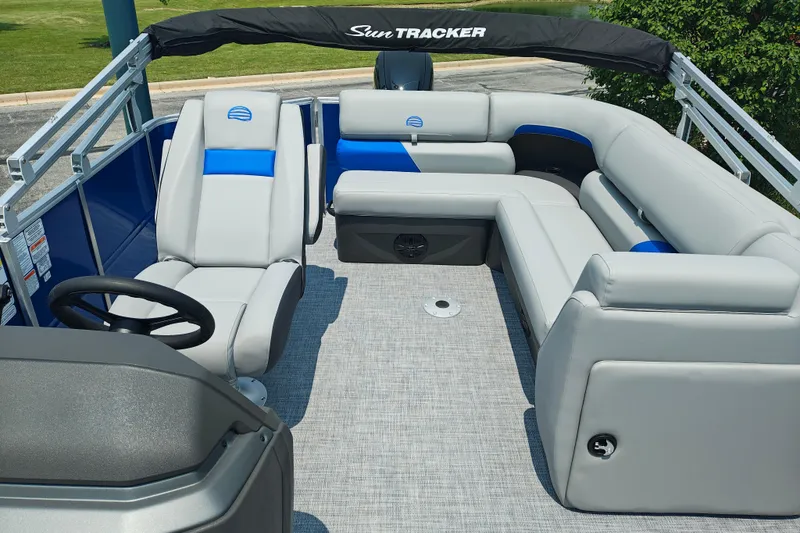 Slide: The Image of 2026 Sun Tracker Party Barge 20 DLX interior with gray and blue seating, steering wheel, and canopy. - 10